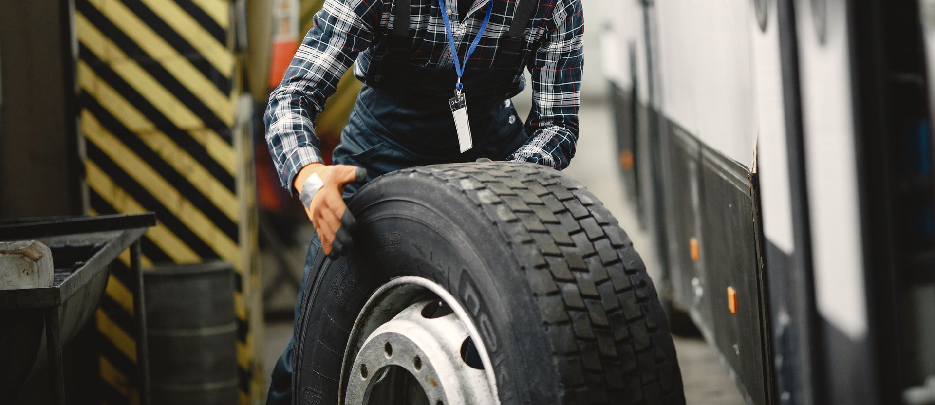 Auto mechanic working indoors in a vehicle repair garage managing a large tire.